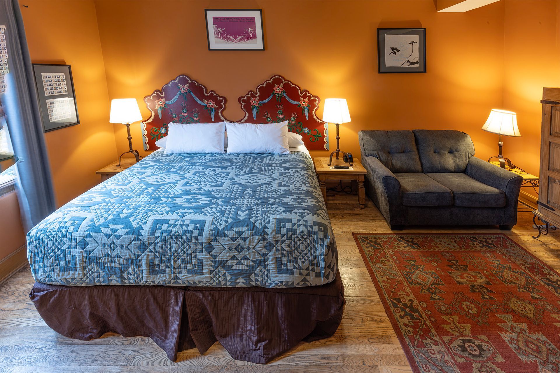 Bedroom with a bed, couch, lamps, rug, and art on orange walls.