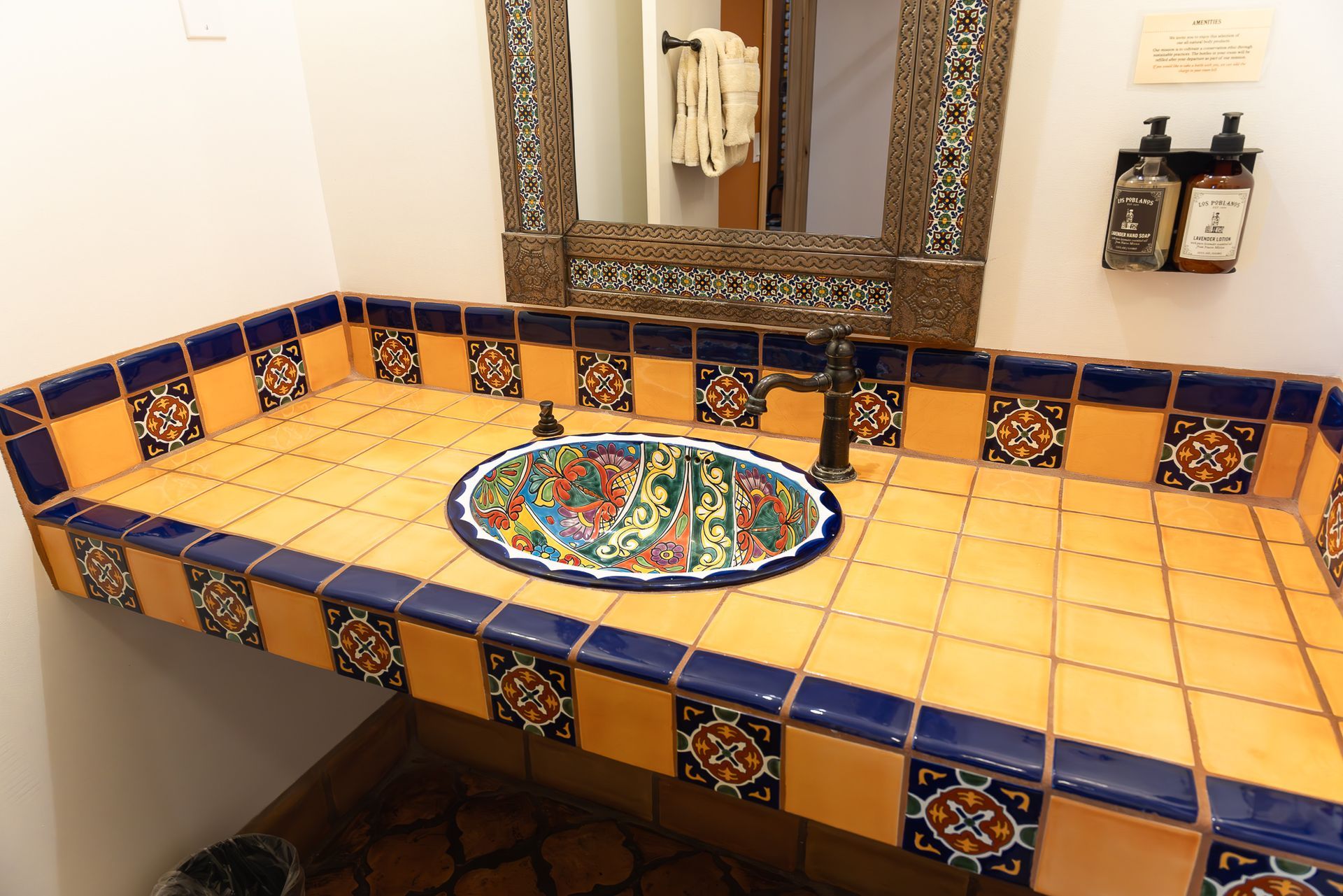 A bathroom sink with an orange tiled countertop and colorful decorative sink basin.