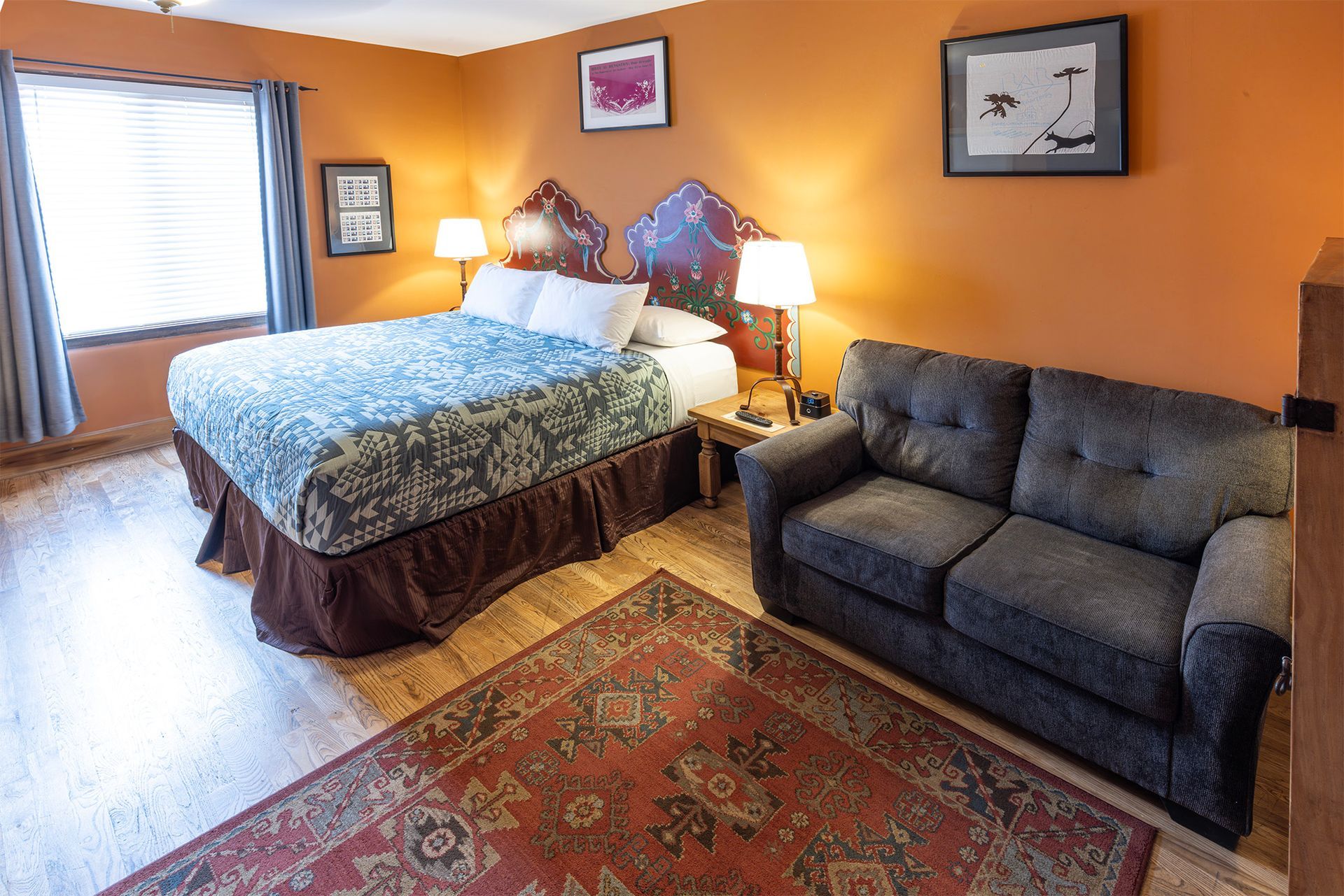 Bedroom with a bed, sofa, rug, and orange walls.