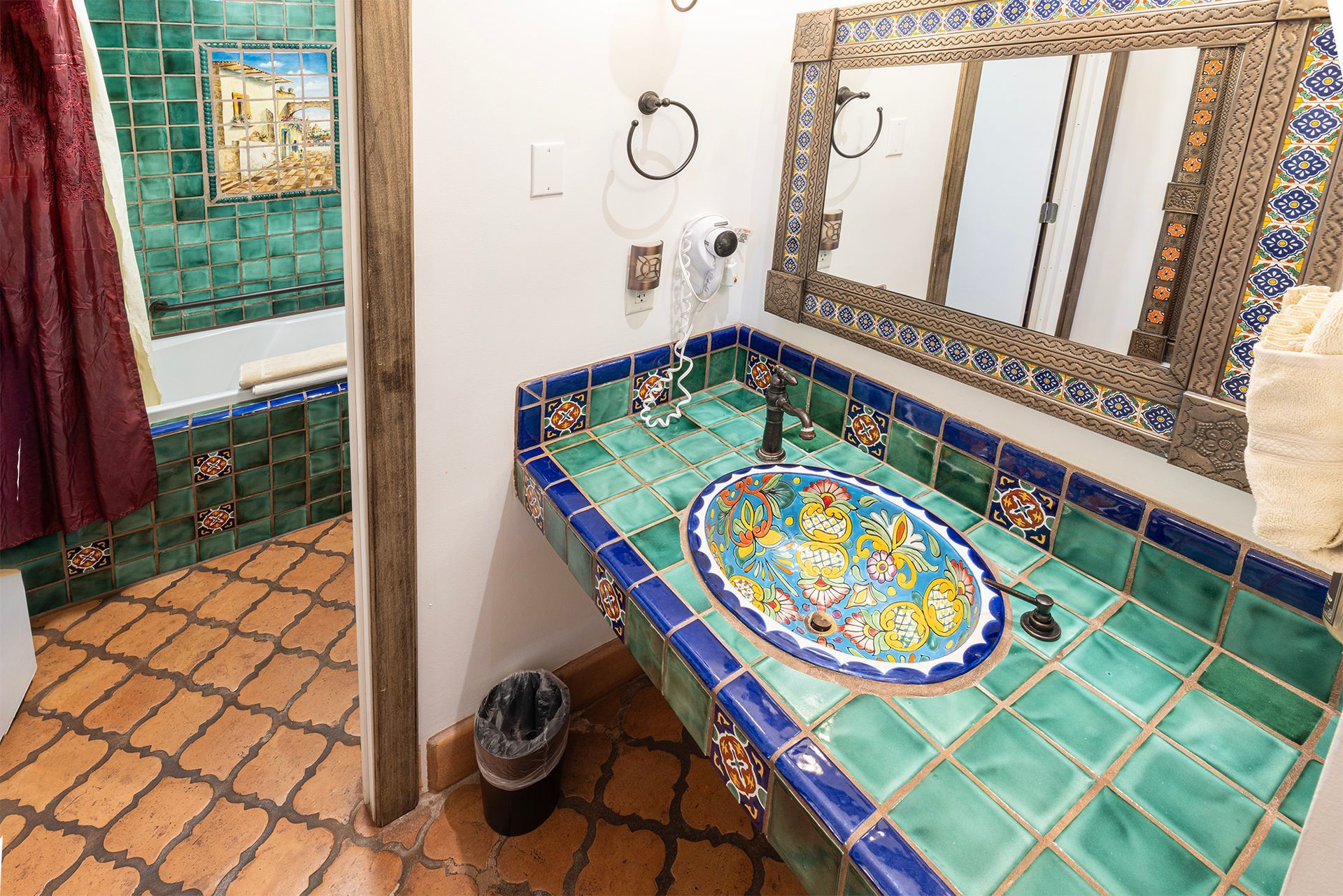 Bathroom with turquoise tiles, patterned sink, ornate mirror, and terracotta floor.