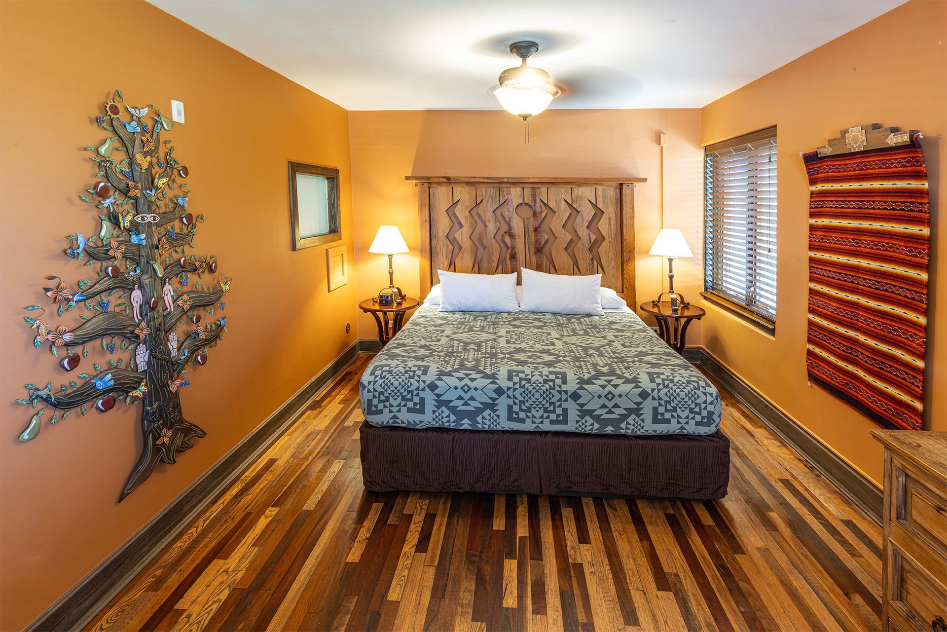 Bedroom with bed, lamps, wall decorations, wood floor, and orange walls.