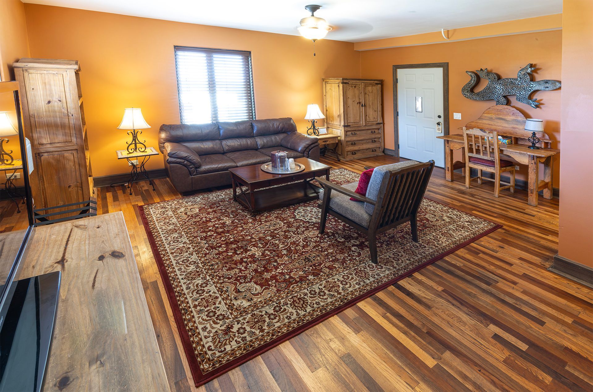 Living room with brown leather couch, area rug, wooden furniture, and orange walls.