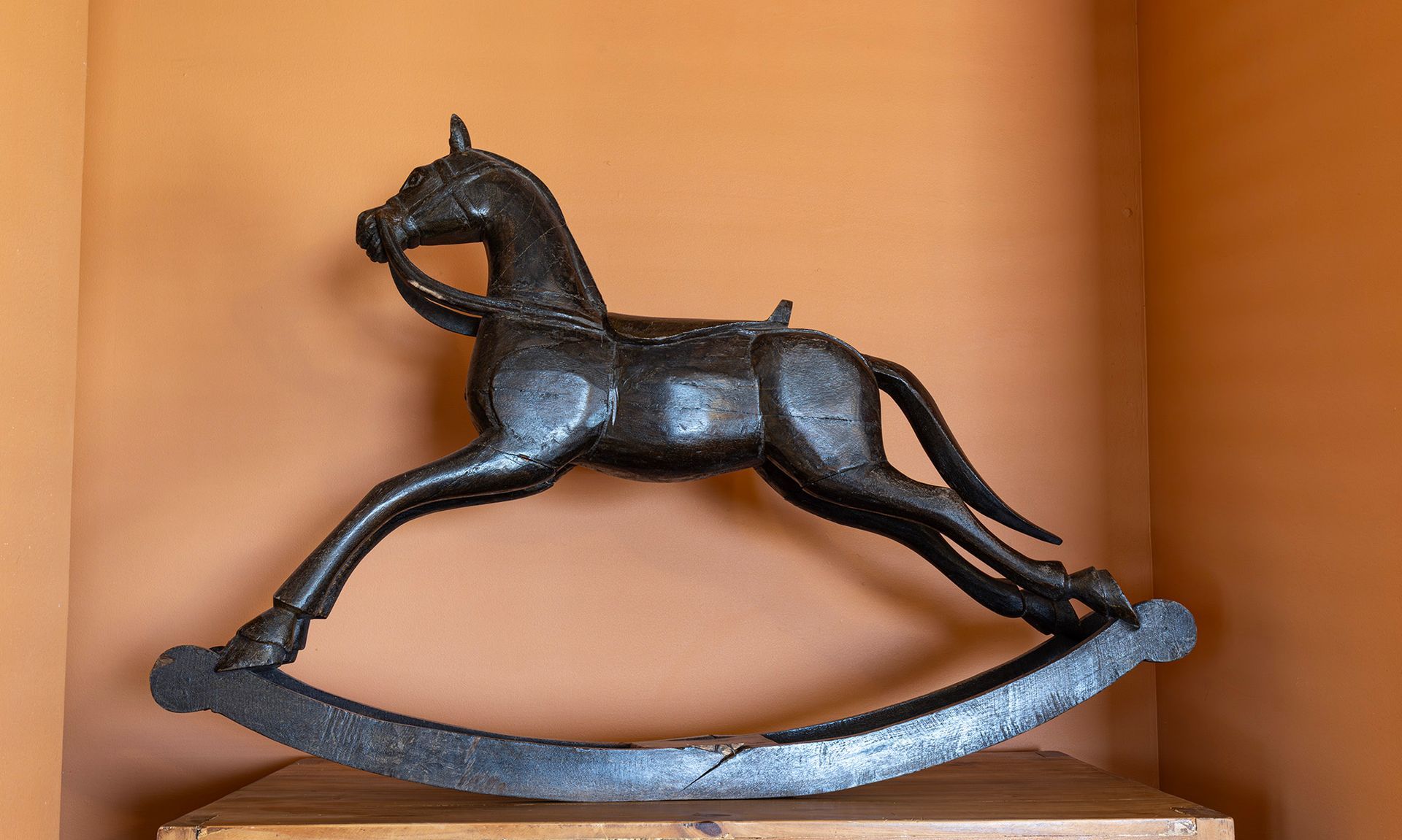 Black cast iron rocking horse against an orange wall.