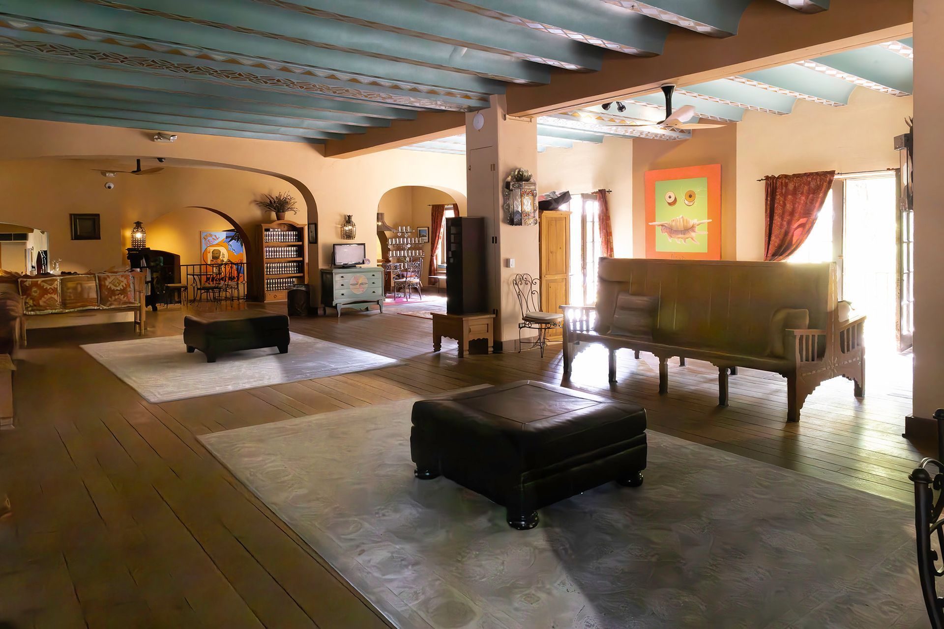Open living area with couches, ottomans, and arched doorways; blue ceiling with exposed beams; warm-toned walls.