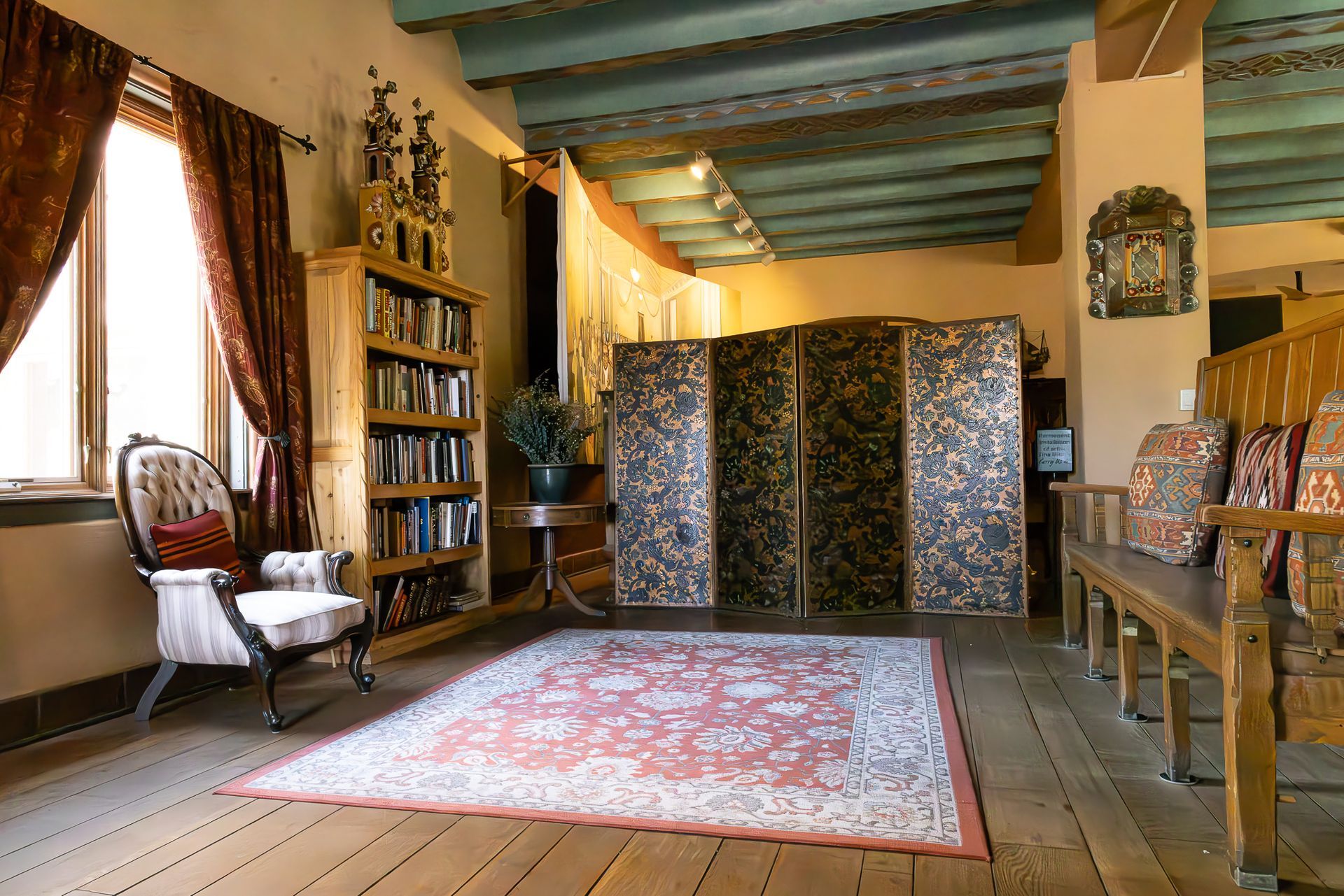 Cozy room with wooden floors, rug, bookcase, screen, and bench. Red curtains, light-colored walls, and a teal ceiling.