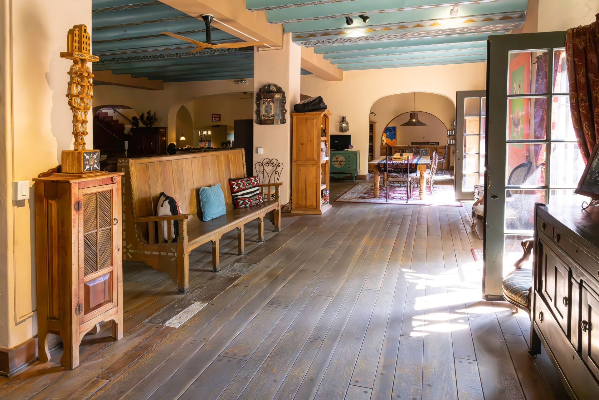 Wooden-floored room with bench, cabinet, and open doorway to dining area. Blue-painted ceiling, reddish walls.