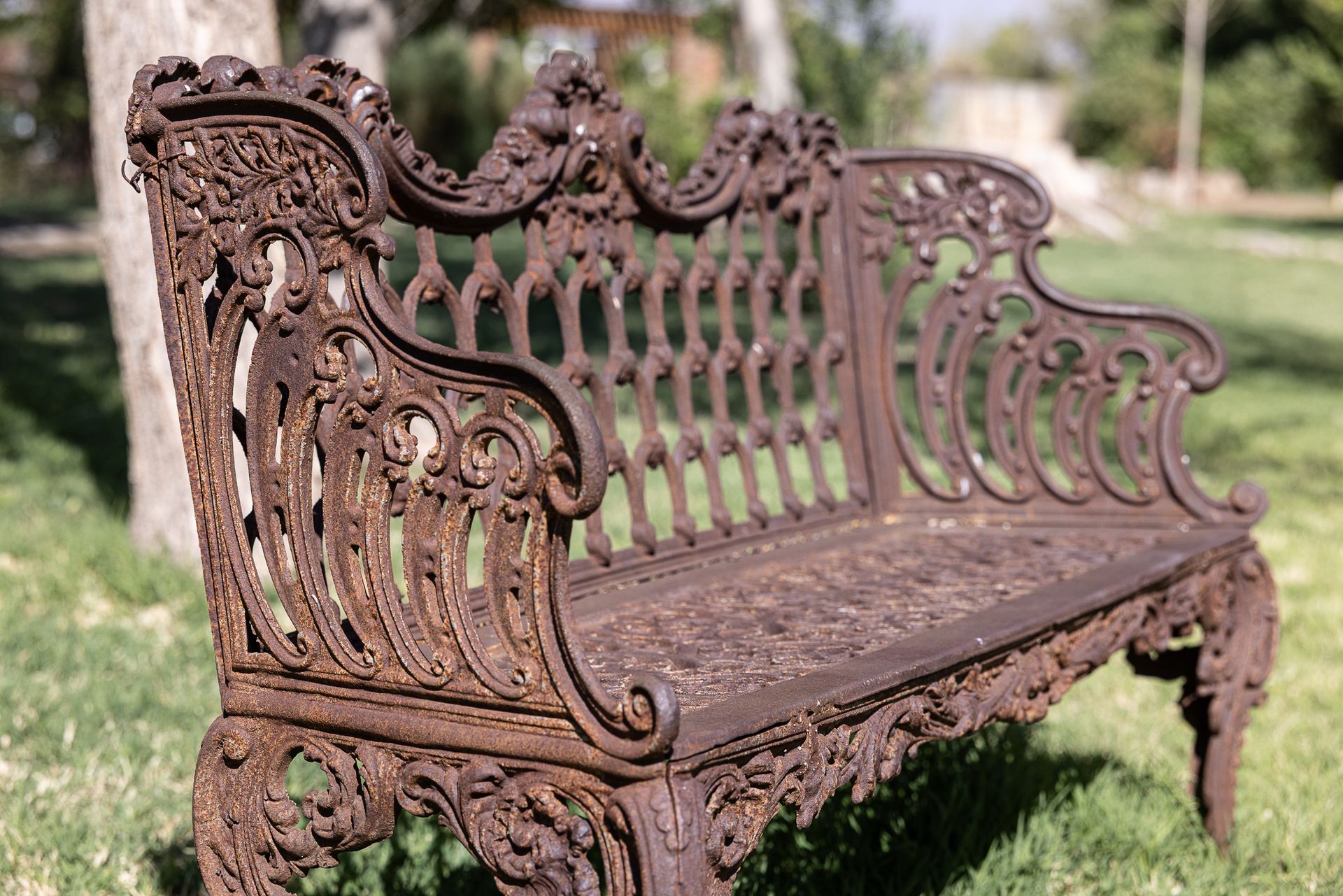 Ornate rusty metal bench on grass in a park.