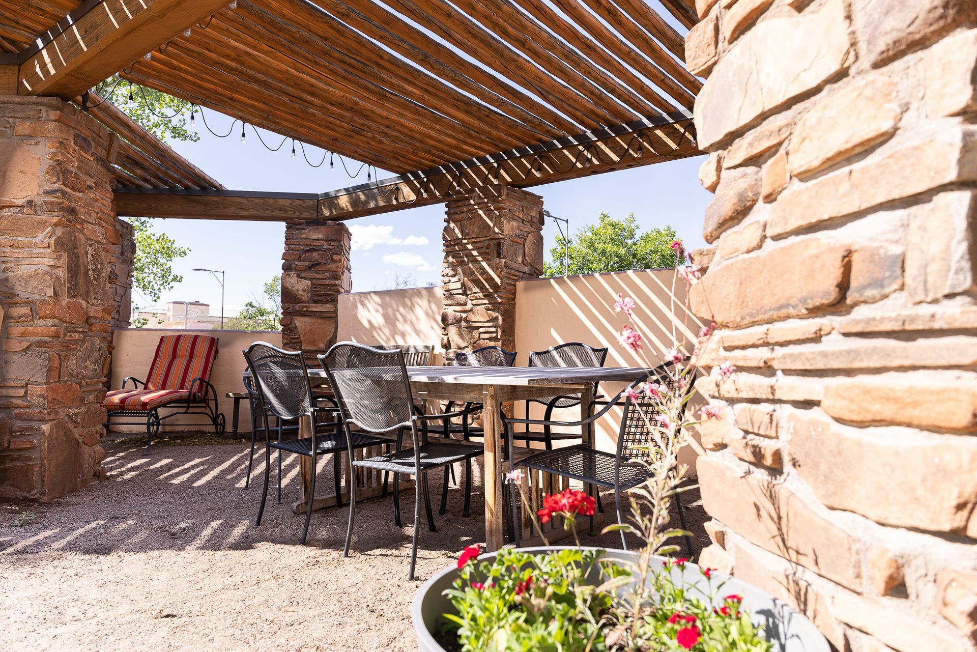 Outdoor patio with stone walls, wooden pergola, table, chairs, and potted flowers.
