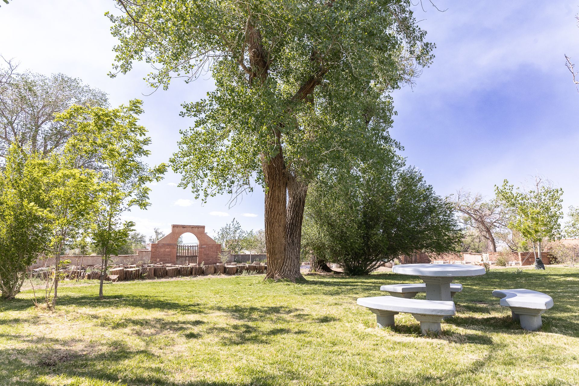 Park with picnic table, large tree, and brick archway under blue sky.