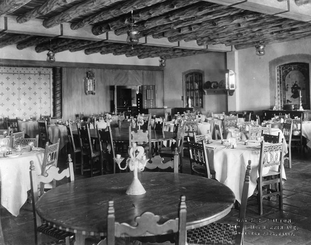Restaurant interior with tables set for dining, rustic chairs, and a beamed ceiling.