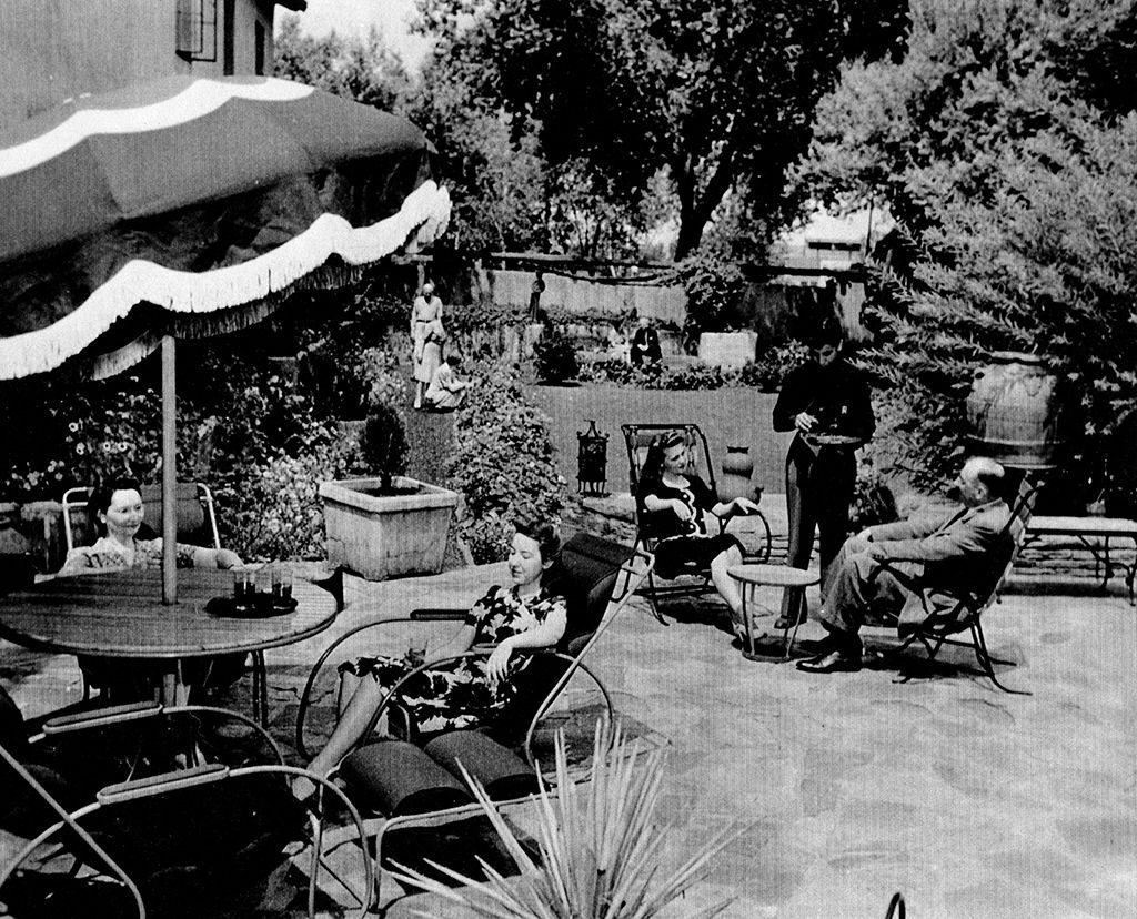 People relax in a sunny, furnished patio with an umbrella.