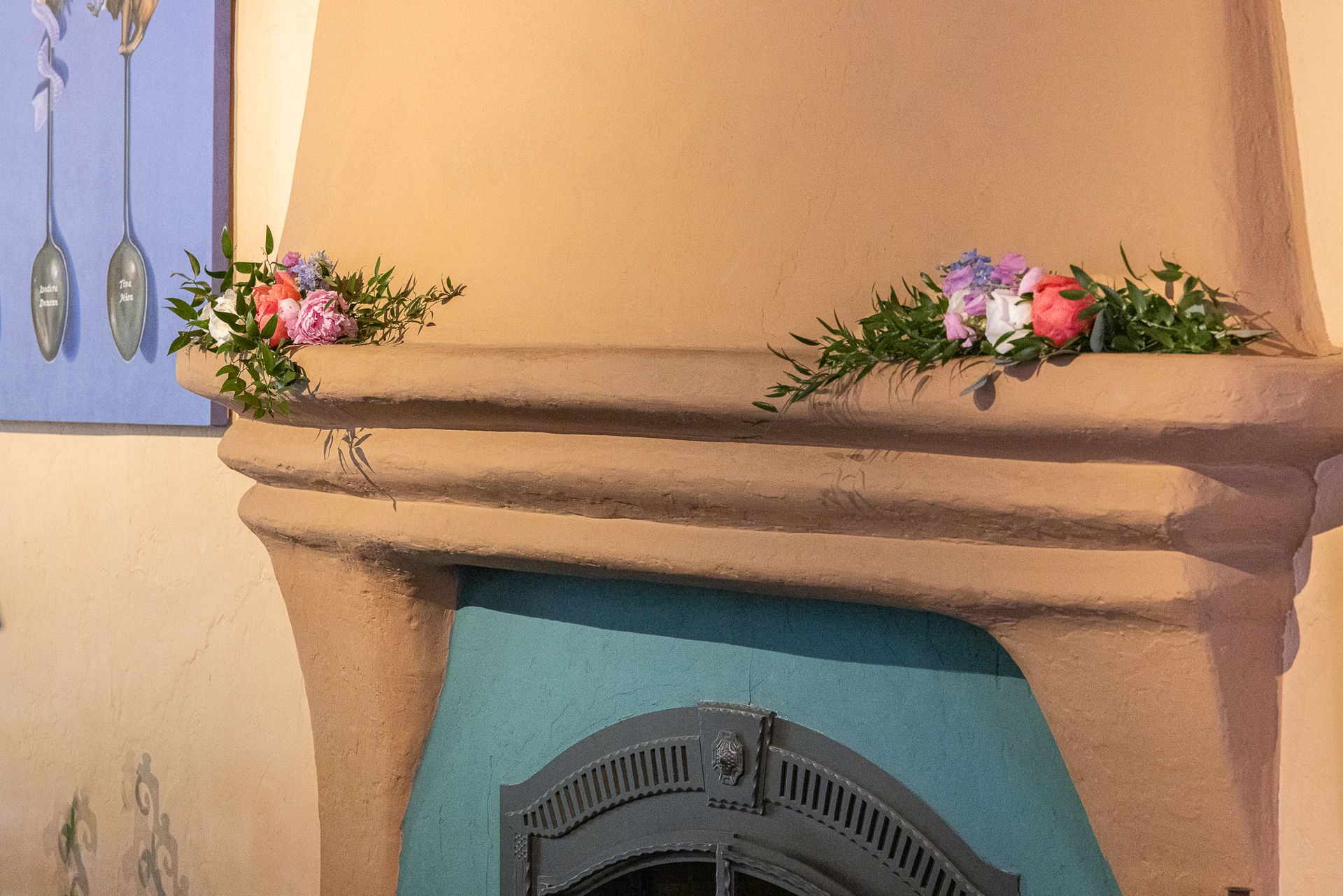 Fireplace with floral arrangement; tan mantle, teal interior, and iron door.