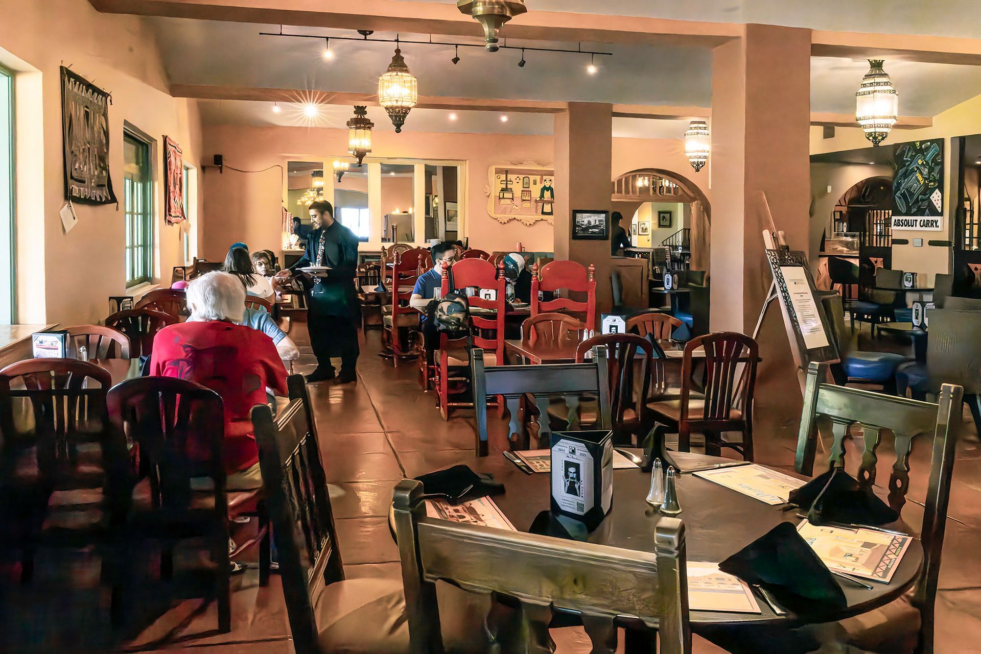 Restaurant interior with patrons seated at wooden tables, server, hanging lanterns, and art on the walls.