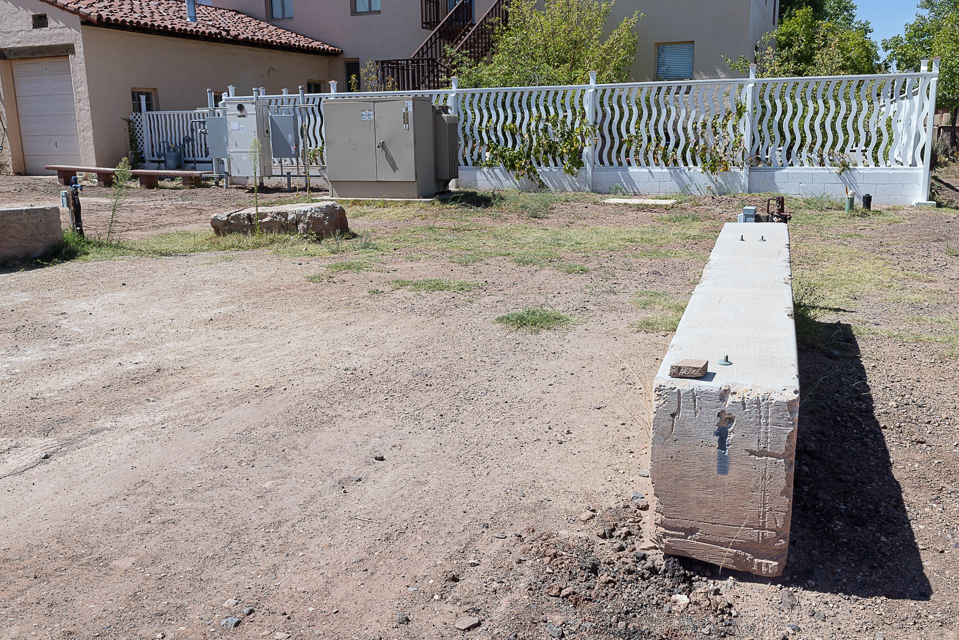 A concrete block and a weathered yard with a white fence and buildings in the background.