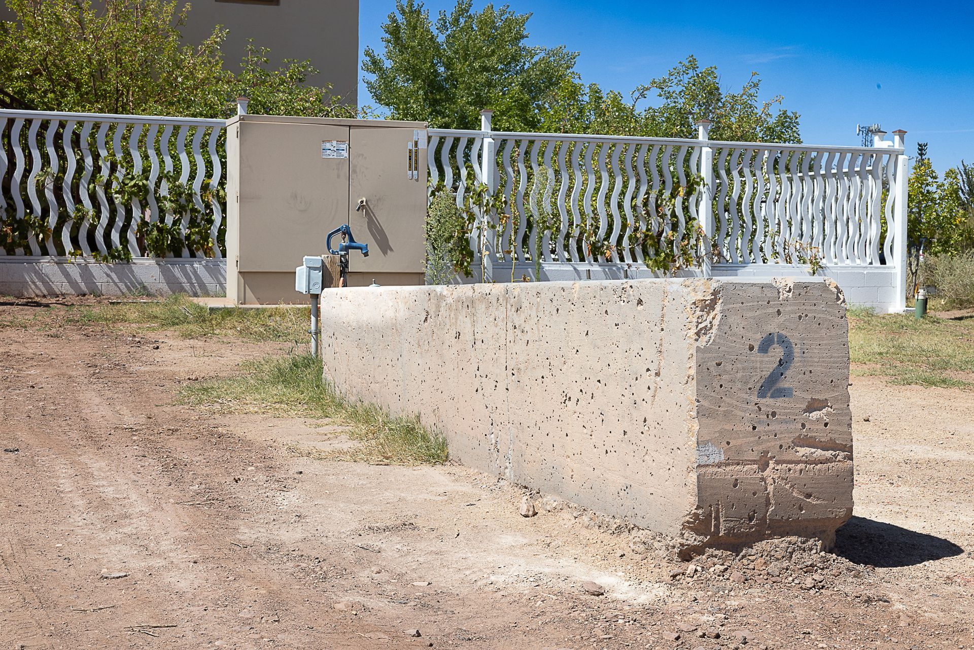 Concrete RV campsite marker #2 with water hookup, set in a dirt lot with a white fence and trees.