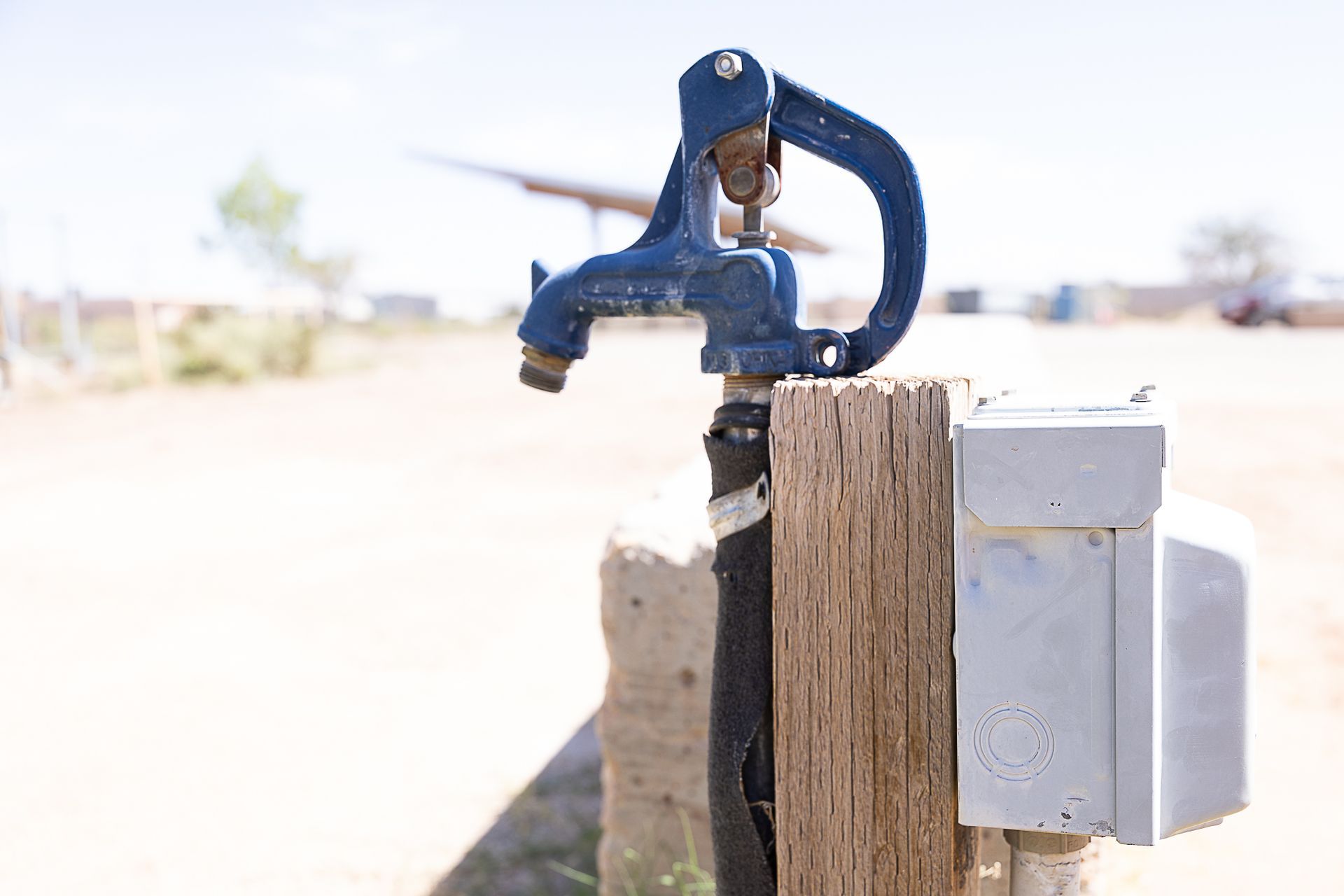 Blue water spigot on a wooden post in a sunny outdoor setting.