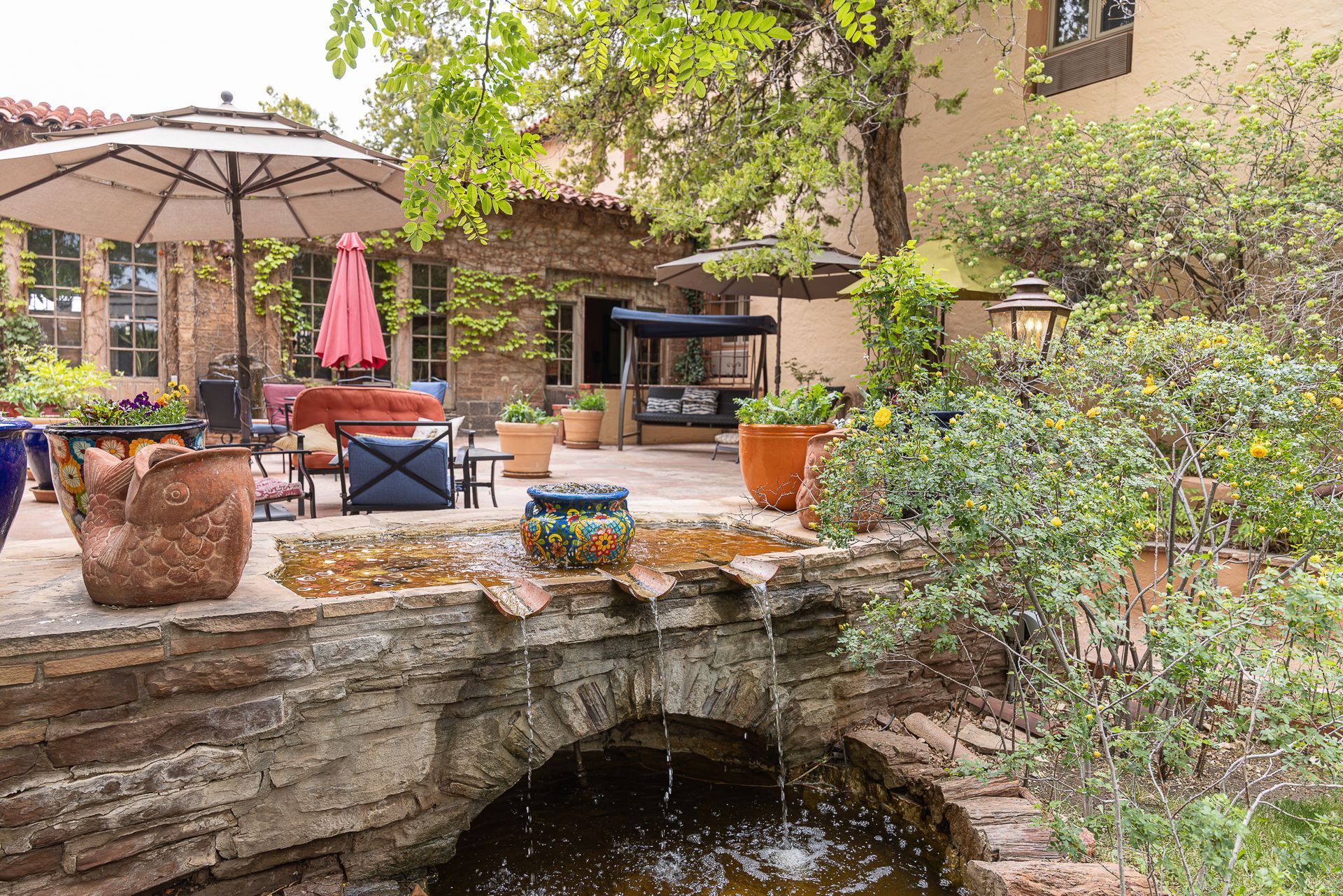 Courtyard with a stone bridge, a patio with a table, and vibrant flowers in pots.