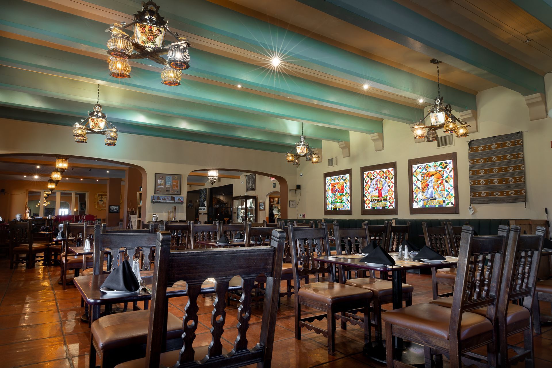 Interior of a Southwestern restaurant: dark wooden chairs and tables, stained glass art, lanterns, and turquoise ceiling.