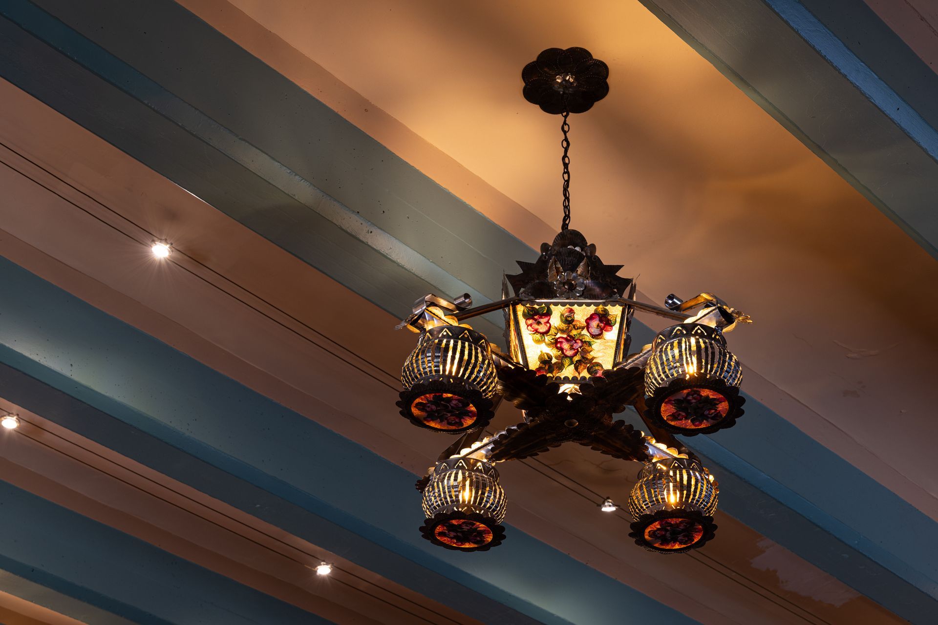 Ornate chandelier hangs from a striped, colorful ceiling; light illuminates decorative details.