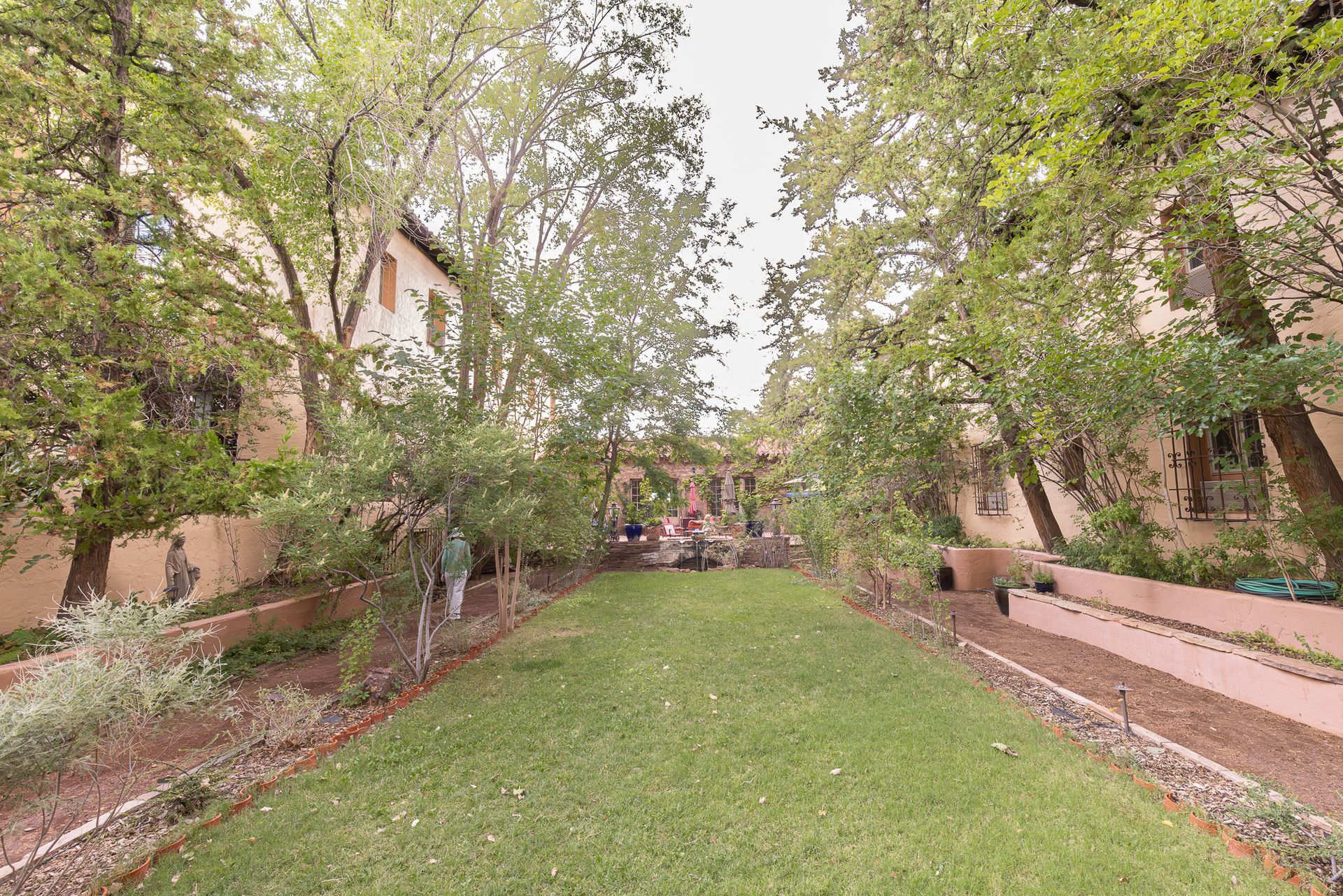 A courtyard with green grass, lined with trees and buildings with tan walls.