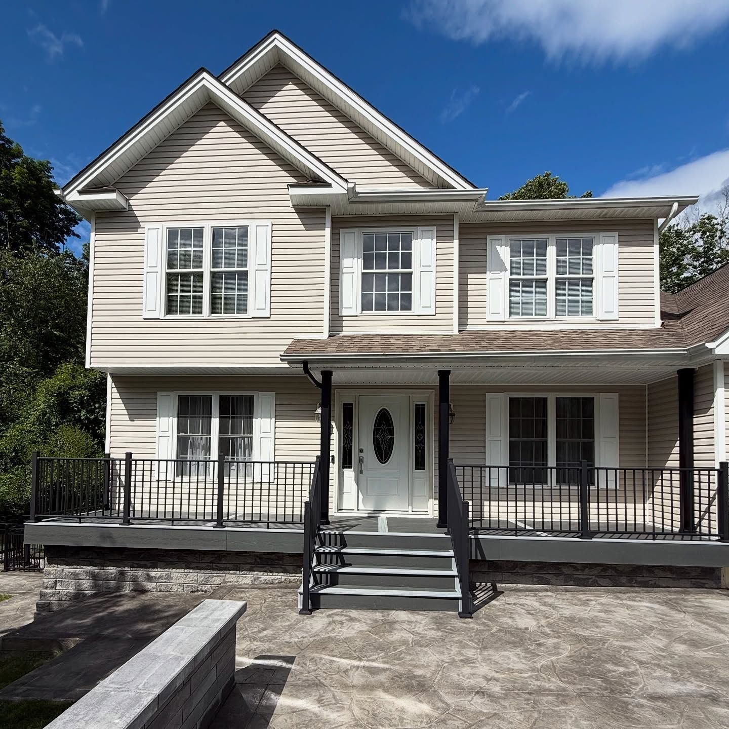 Two-story beige house with white trim, white shutters, and a front porch. Blue sky background.