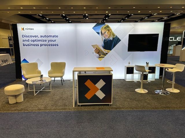 Trade show booth for Nintex, with seating, a monitor, and the company's logo and tagline.