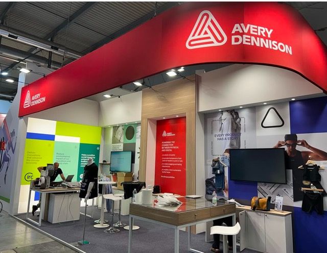 Avery Dennison trade show booth with red and white branding. People stand and work in the open space.