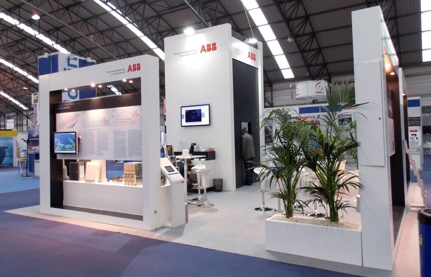 ABB trade show booth with displays, screens, and plants, in a large venue.