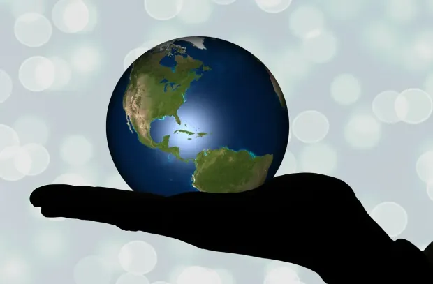 Silhouette hand holding a glowing blue and green Earth globe against a blurred background.