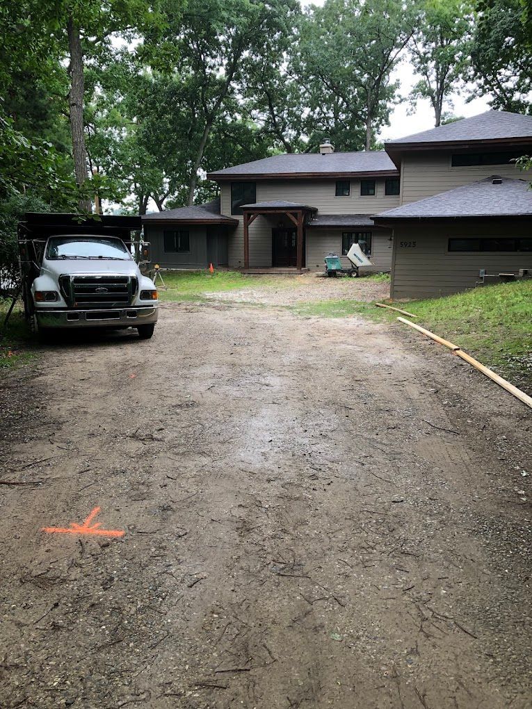 A truck is parked in a dirt driveway in front of a house.