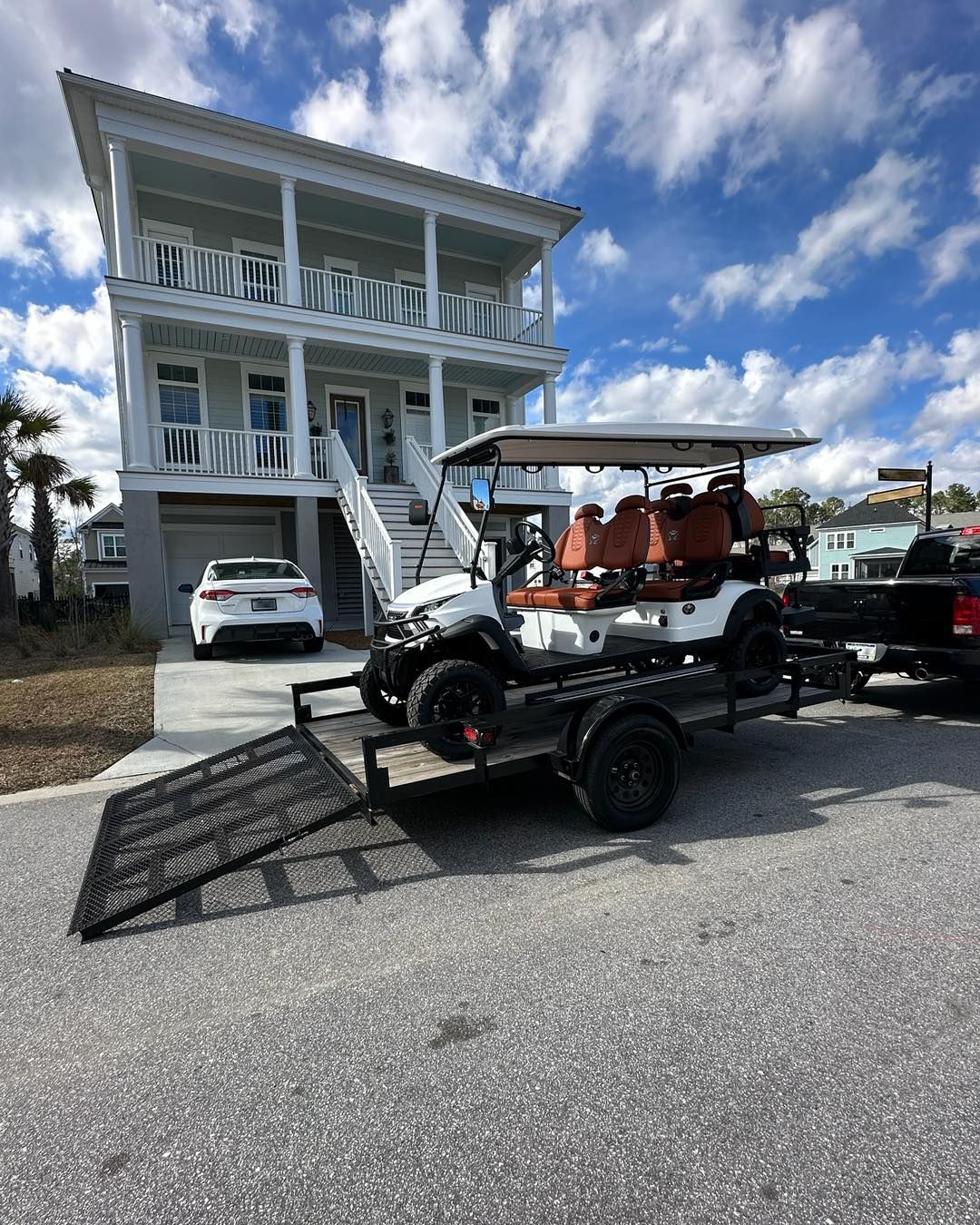 A golf cart is being towed to a house on a trailer.