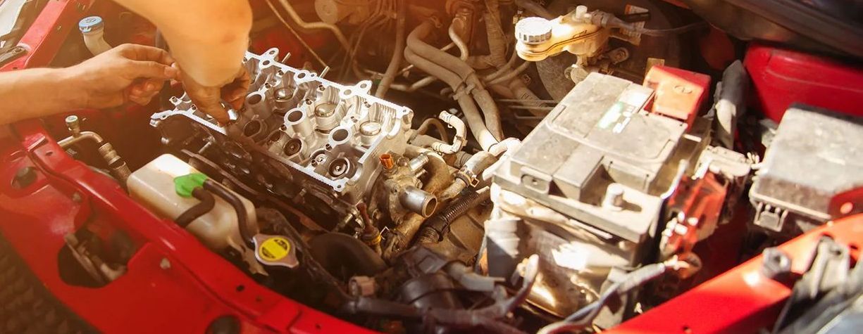 A man is working on the engine of a red car.