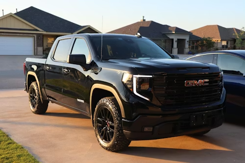 A black GMC Sierra pickup truck parked on a driveway in front of suburban houses.