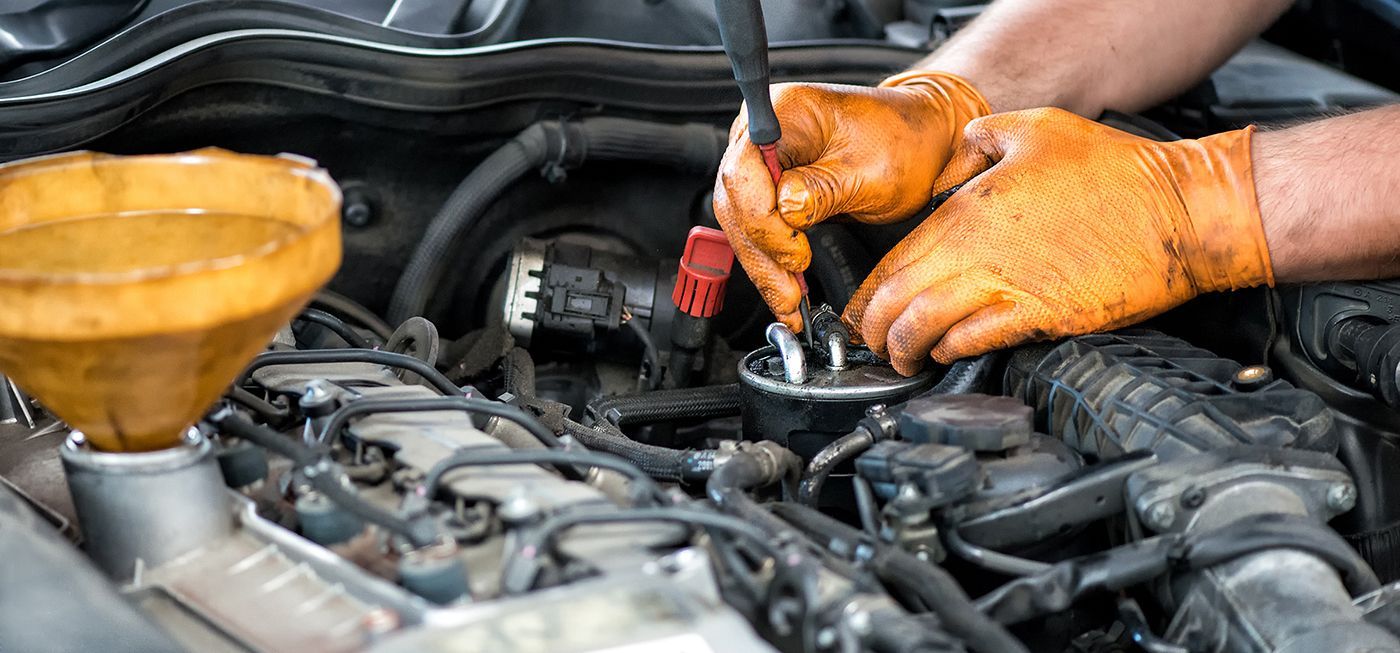 Mechanic in orange gloves checks engine with oil funnel nearby