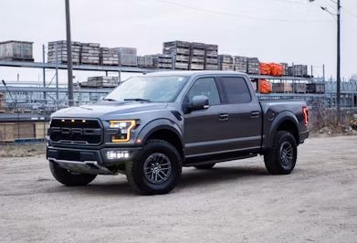Dark gray pickup truck parked on a lot, with an industrial building in the background