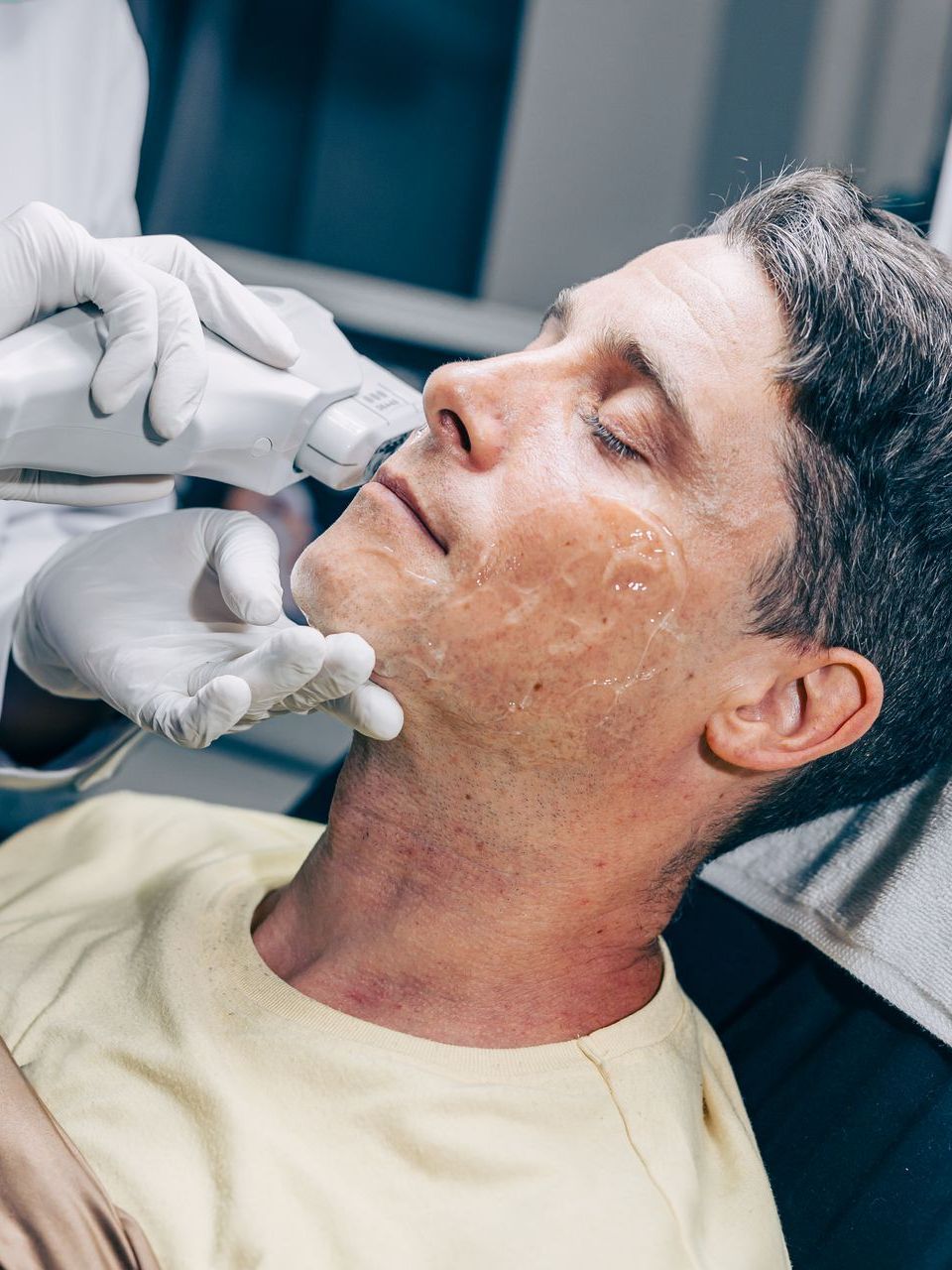 a man in a yellow shirt is getting a treatment on his face
