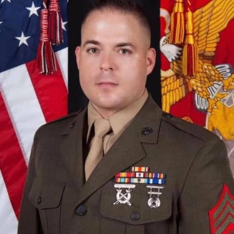 A man in a military uniform stands in front of an american flag