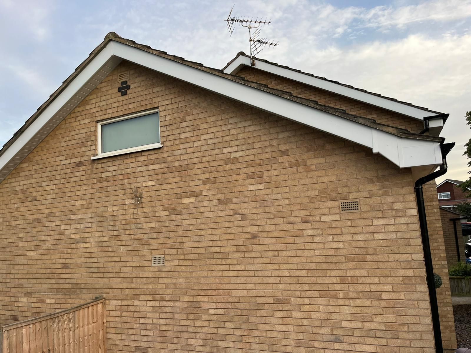 Brick building exterior with gable roof, window, and antenna.
