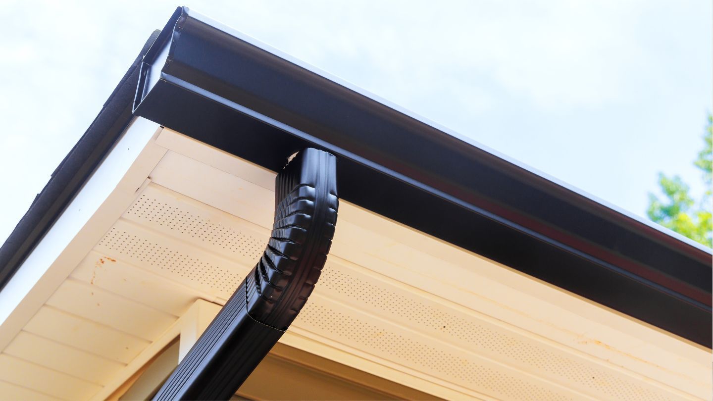 Black gutter and downspout on a cream-colored house with a white soffit.