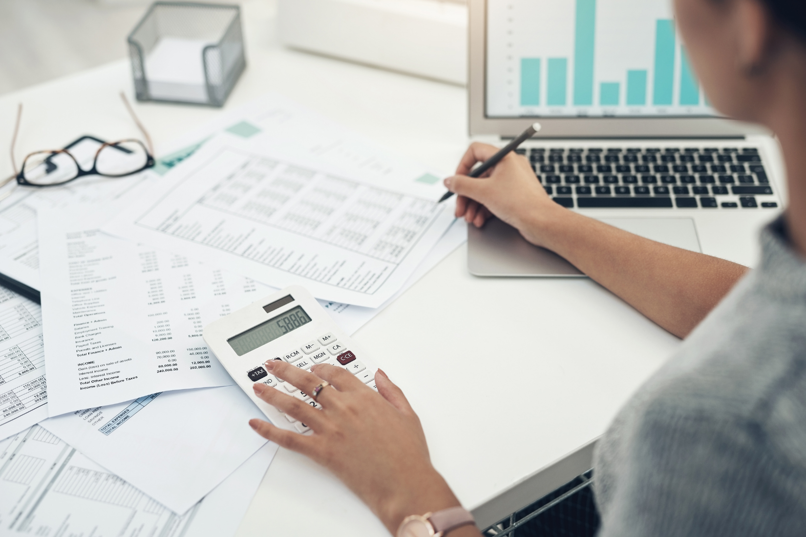 A Virtual Assistant is sitting at a desk using a calculator and a laptop.