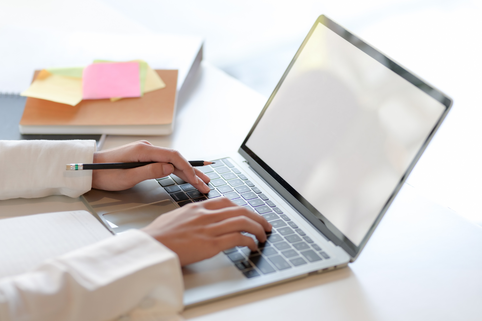 A Virtual Assistant is typing on a laptop computer with a pen.