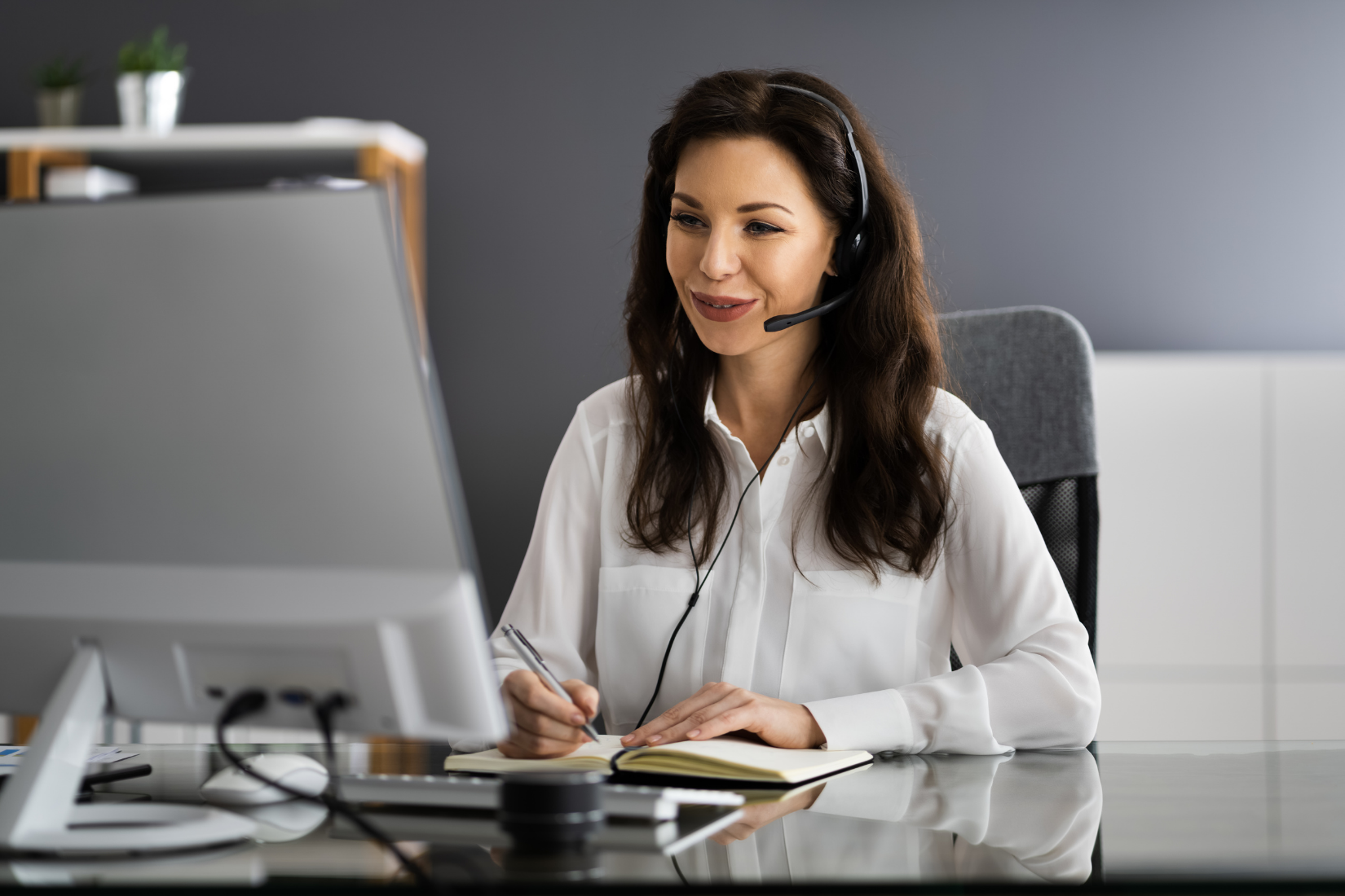 A Virtual Assistant wearing a headset is sitting at a desk in front of a computer.