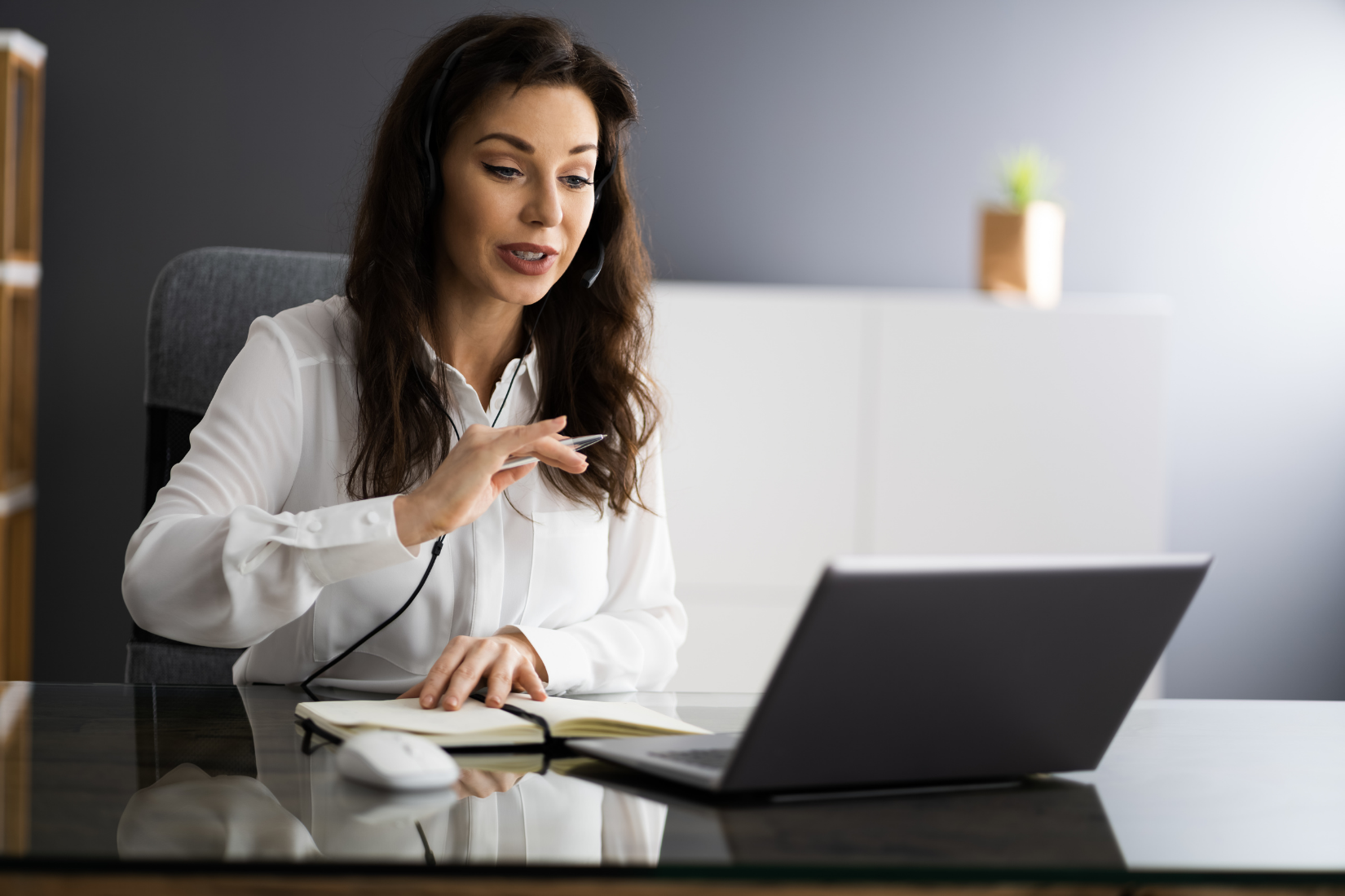 A Virtual Assistant is sitting at a desk using a laptop computer while wearing a headset.