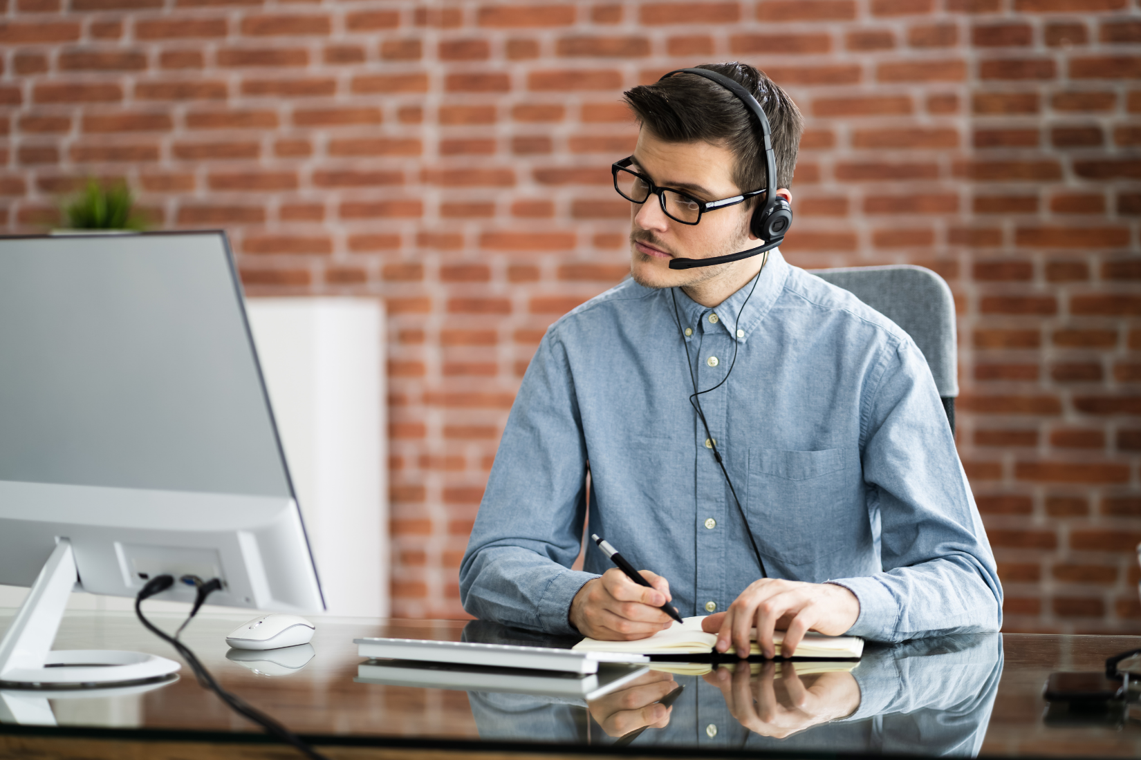 A Virtual Assistant wearing a headset is sitting at a desk in front of a computer.