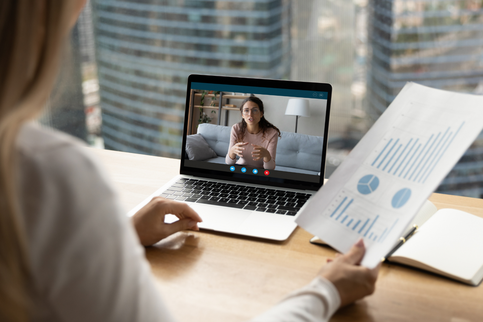A Virtual Assistant is sitting at a desk holding a piece of paper in front of a laptop computer.