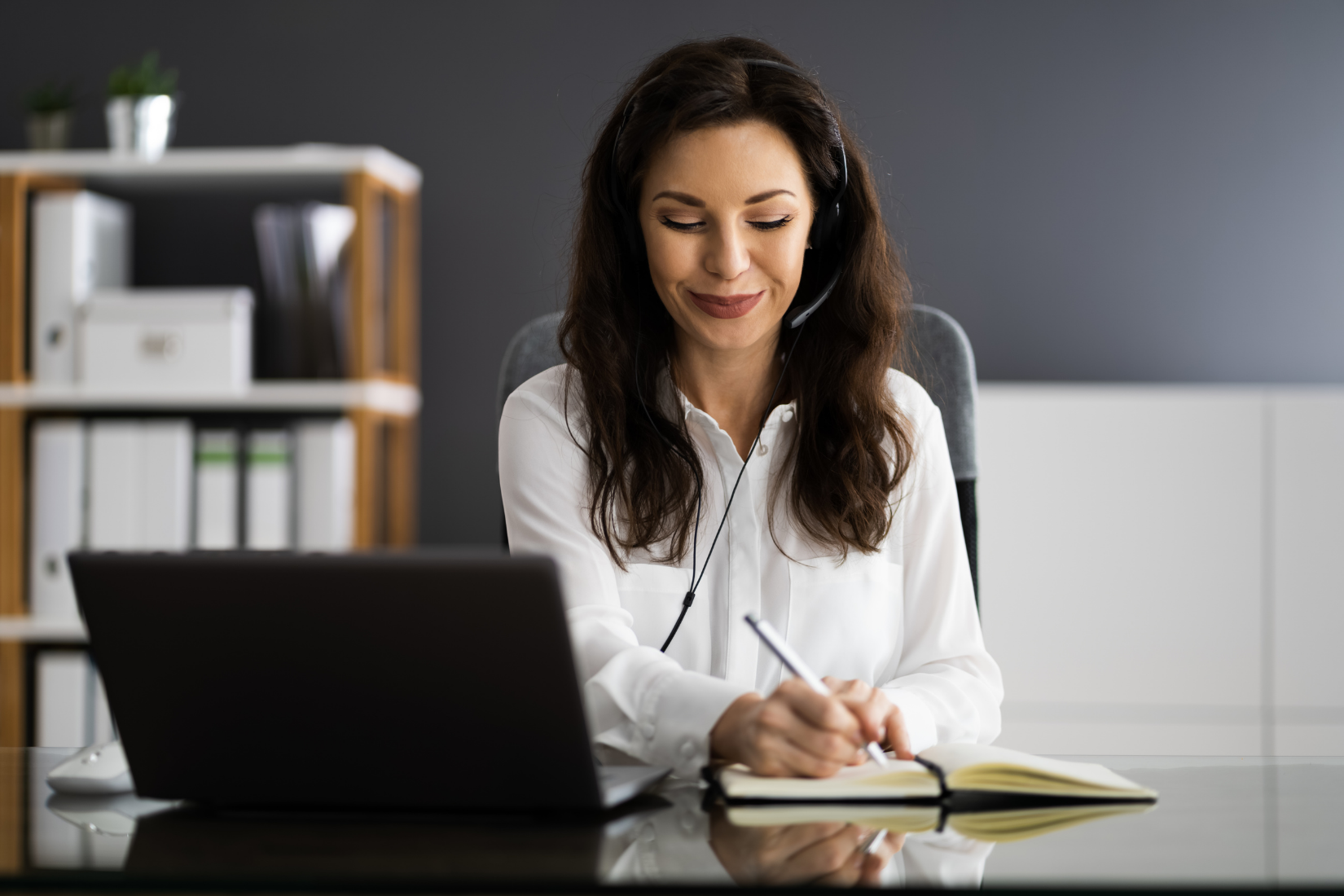 A Virtual Assistant wearing a headset is sitting at a desk in front of a laptop computer.