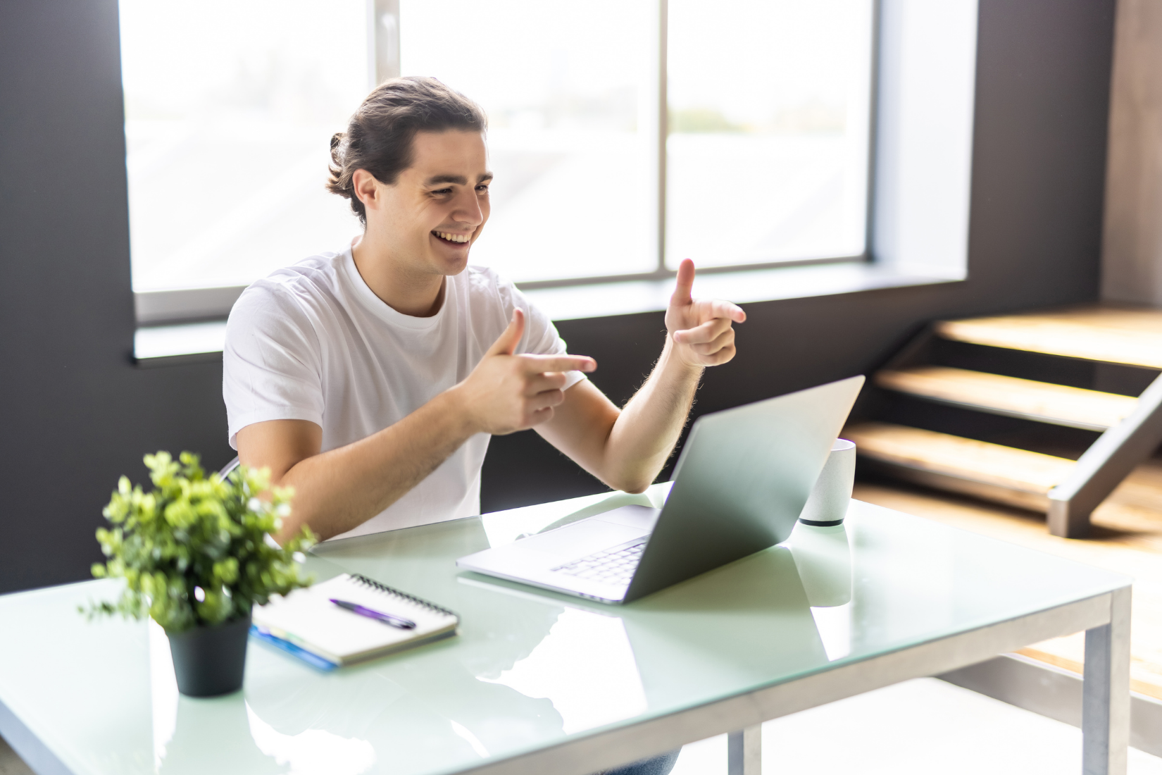 A Virtual Assistant is sitting at a desk with a laptop and giving a thumbs up.