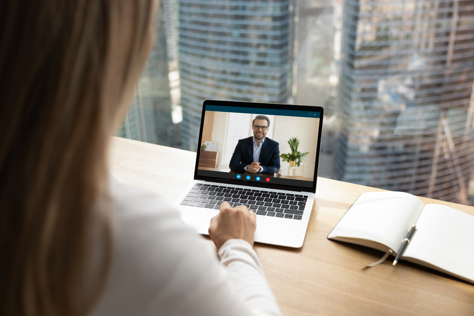 A Virtual Assistant is sitting at a desk using a laptop computer to have a video call with a man.