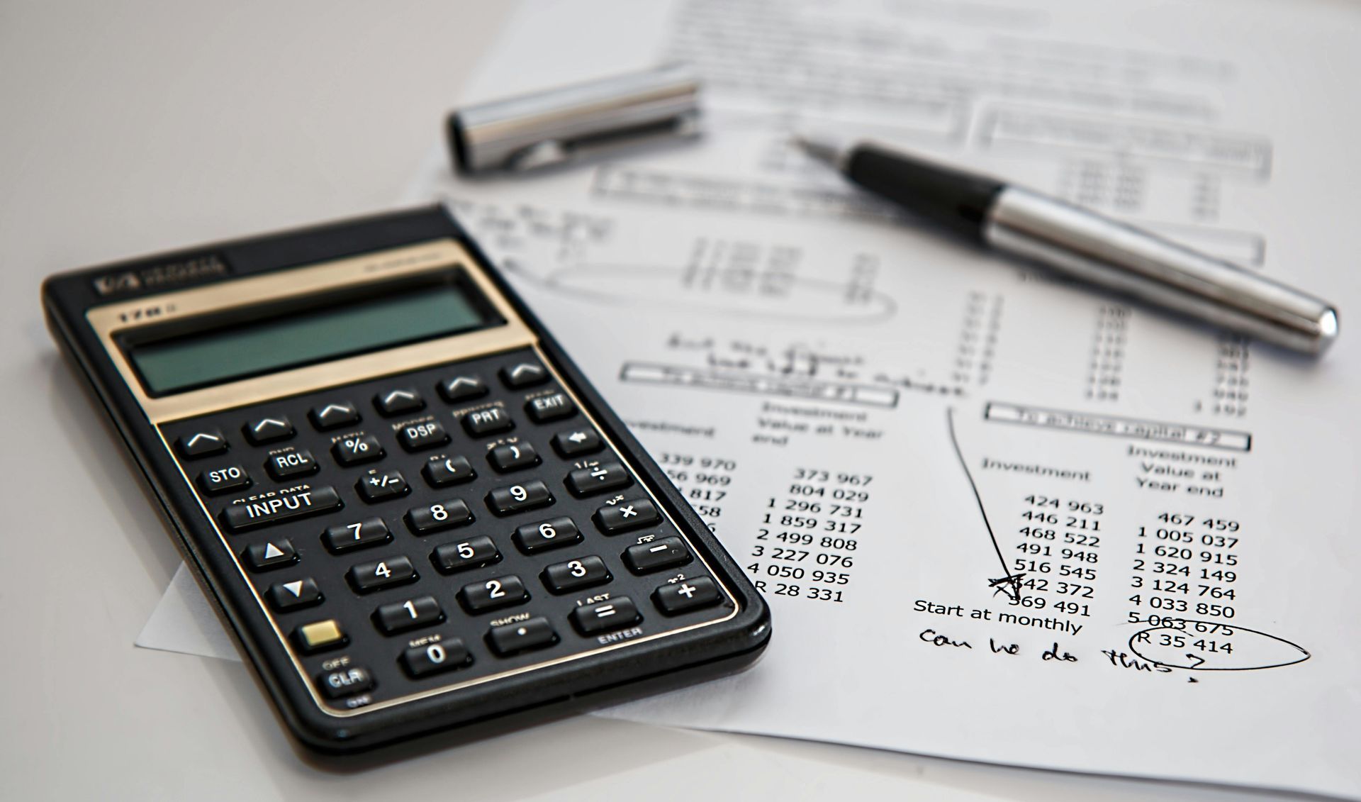 Calculator, pen, and financial documents on a white surface, suggesting accounting or calculations.
