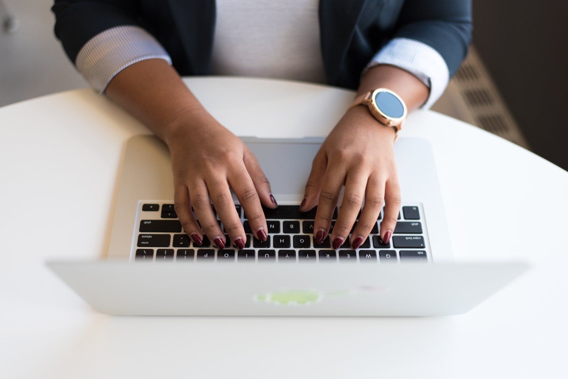 A Virtual Assistant is typing on a laptop computer while wearing a watch.